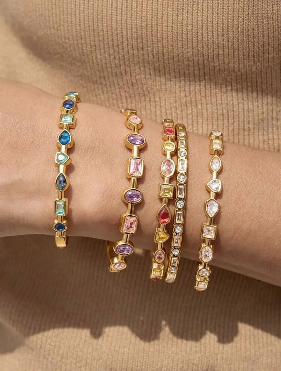 Cinco brazaletes dorados con piedras de colores y circonias en la muñeca