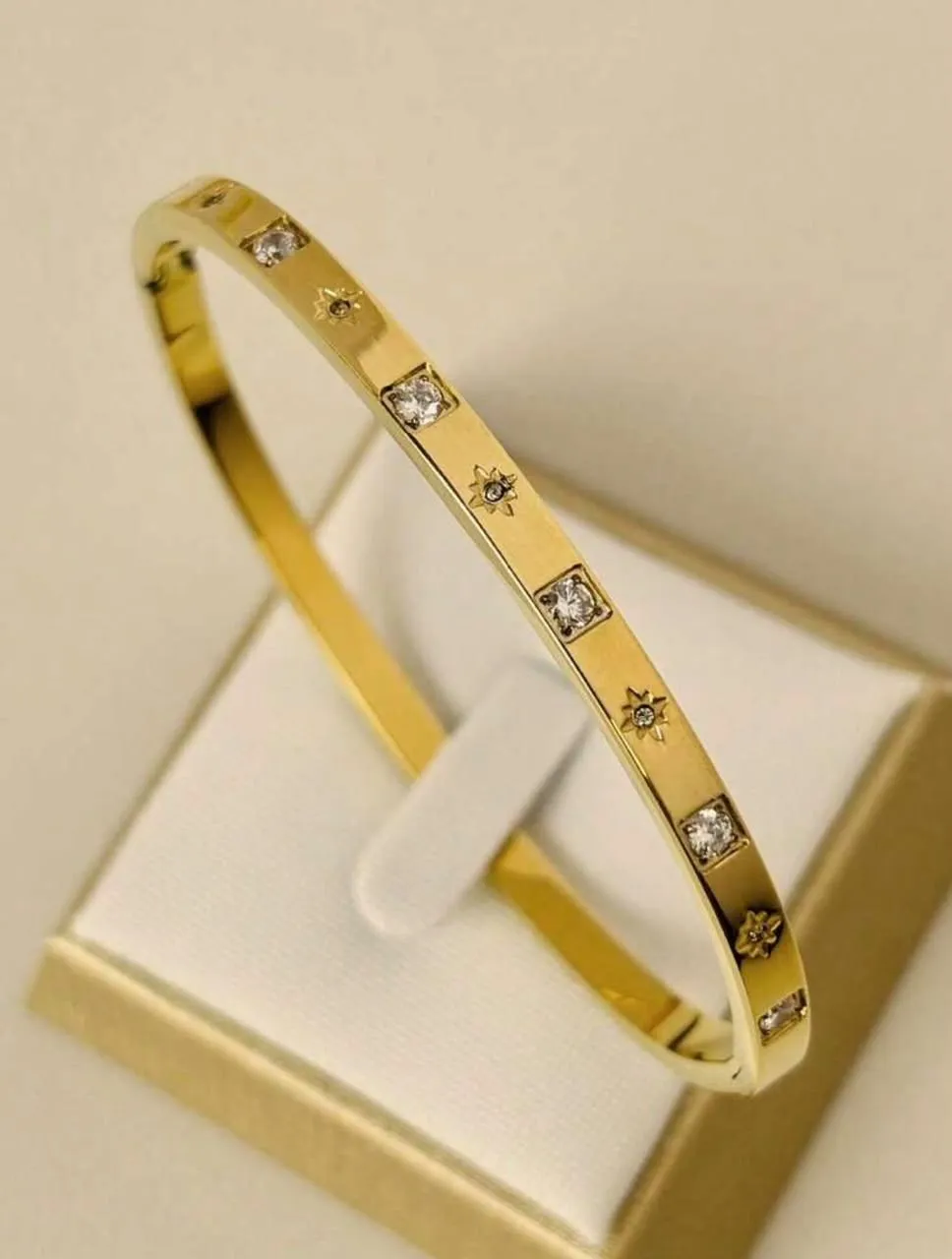 Brazalete dorado con circonias y estrellas grabadas en su estuche de presentación
