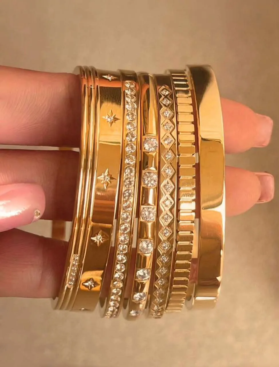 Mano sosteniendo un set de siete brazaletes dorados apilables con distintos diseños